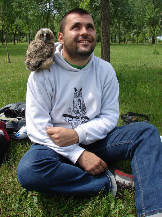 Milan Ruzic sitting on the ground with a baby owl on his shoulder